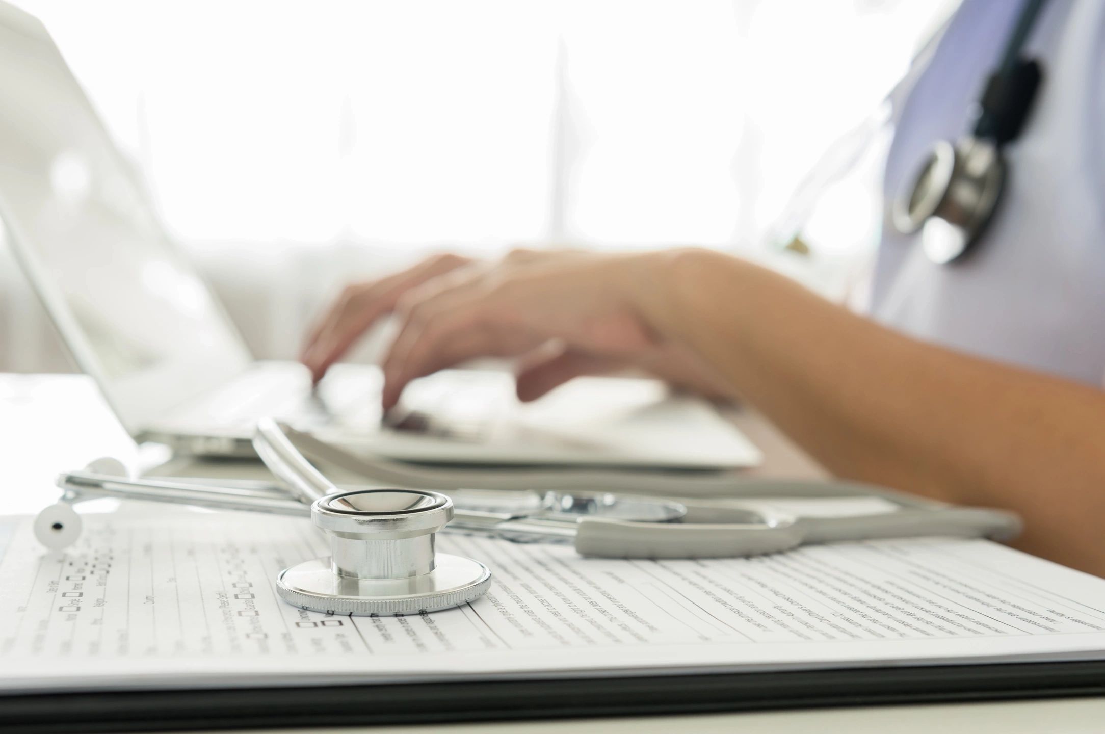 Woman typing on a keyboard with a stethoscope in the foreground